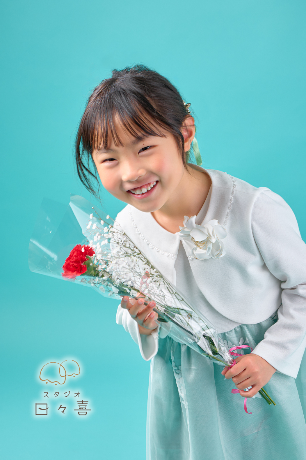 お花を持ってカメラを覗き込むようにニッコリとはにかむ女の子のアップ写真。光に包まれた透明感のある表情が印象的な一枚。