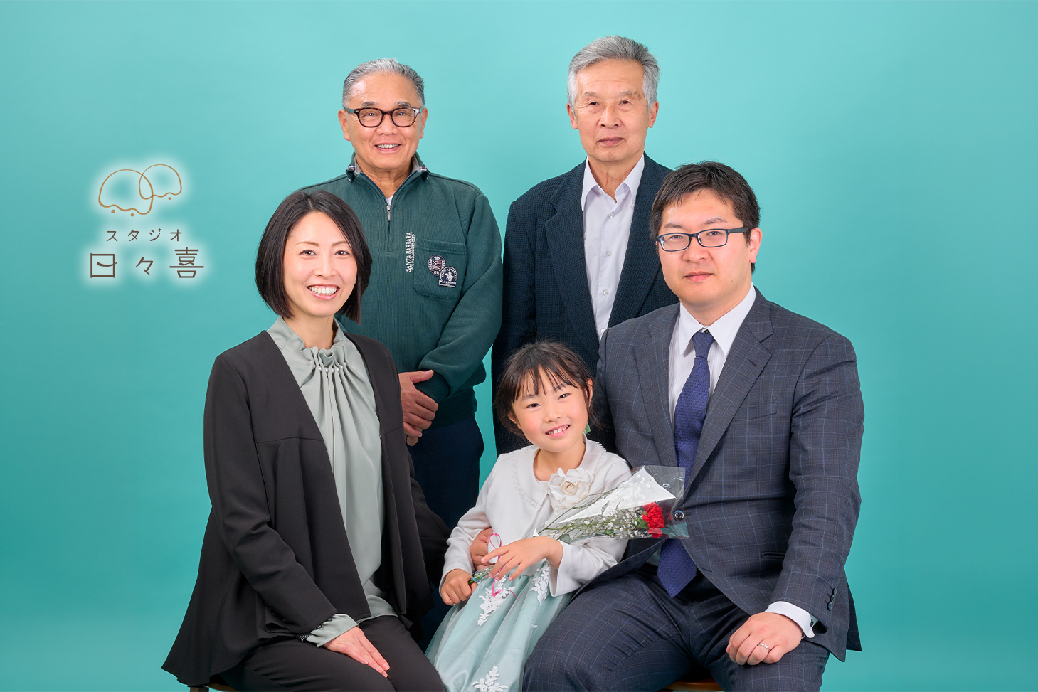 卒園記念の家族集合写真。主役の女の子を囲んで、お父様、お母様、おじい様の三世代5名が温かい笑顔で並んでいるスタジオポートレート。